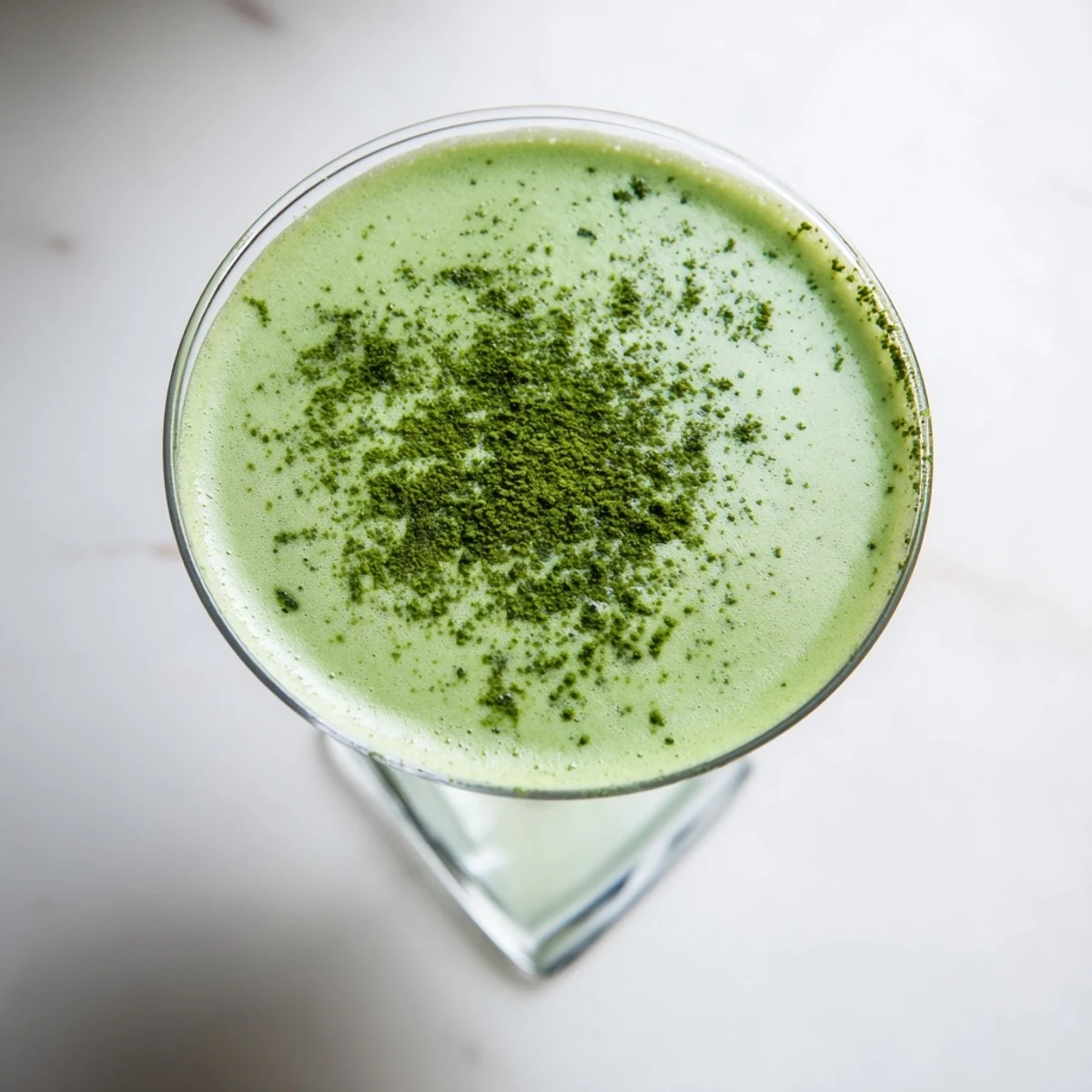 A frothy Matcha Martini cocktail in a chilled glass, topped with a dusting of earthy green tea powder.  