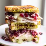 Close-up of a warm, perfectly toasted Pesto Cranberry Turkey Grilled Cheese Melt, sliced in half.