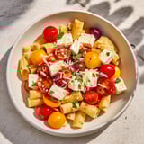 A close-up of creamy Baked Feta Snowfall Cherry Tomato Christmas Pasta, garnished with fresh basil and Parmesan.