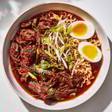 A steaming bowl of Chaos Cooking Birria Ramen, a fusion of spicy beef and ramen noodles.