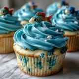 Hand-decorated vanilla cupcakes with blue buttercream and adorable fondant fish toppers for a Pisces-inspired dessert.