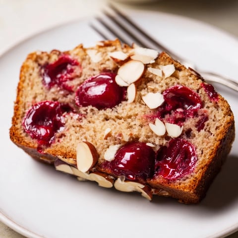 A warm slice of Cherry Almond Loaf Cake, showing juicy cherries baked inside.