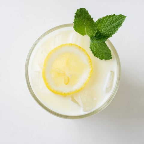 A refreshing glass of Creamy Lemonade Drink garnished with mint and lemon slices over ice, perfect for summer gatherings.  