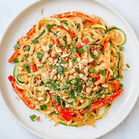 Beautiful bowl of Zesty Peanut Zucchini Noodles: spiralized zucchini with a peanut sauce and peanuts.