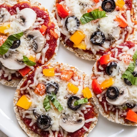 Golden, bubbly rice cake pizza squares topped with melted cheese and fresh basil, a delicious snack.