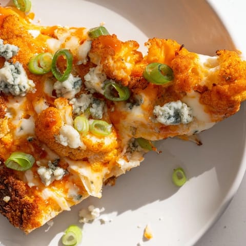 A close-up view of a slice of Buffalo Cauliflower Pizza, garnished with fresh green onions and optional blue cheese crumbles.  