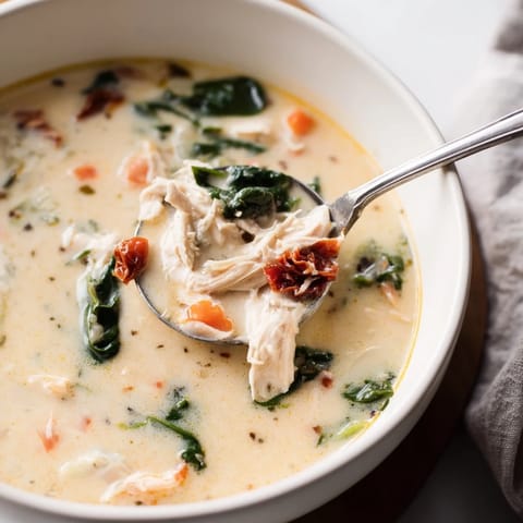 Vibrant, creamy Tuscan chicken soup with tender chicken, bright spinach, and chopped sun-dried tomatoes, garnished with Parmesan.