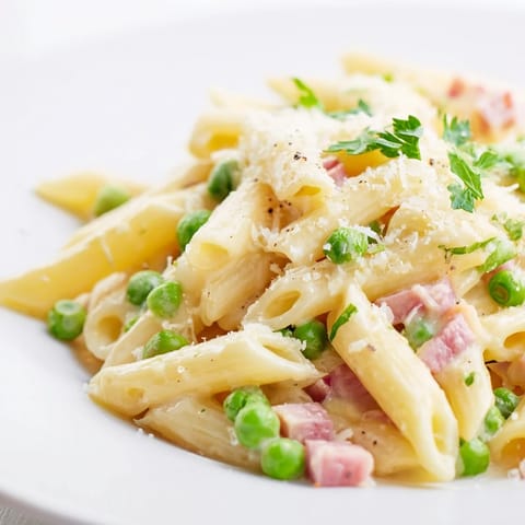Spring Pea & Ham Pasta served in a white bowl, highlighting bright green peas and golden ham in a rich Parmesan sauce.  