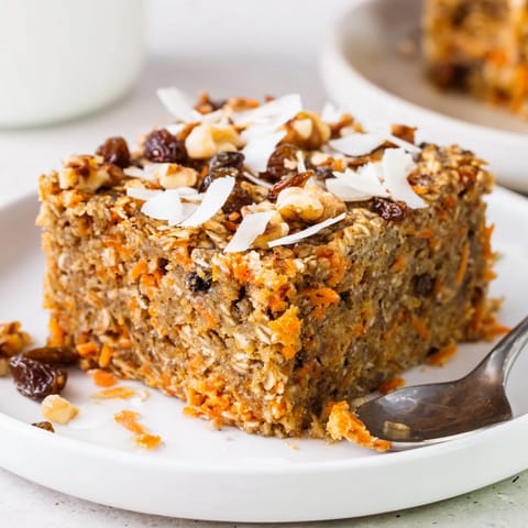 Moist and fragrant slice of Carrot Cake Baked Oatmeal served on a white plate, topped with a dollop of Greek yogurt and maple syrup.