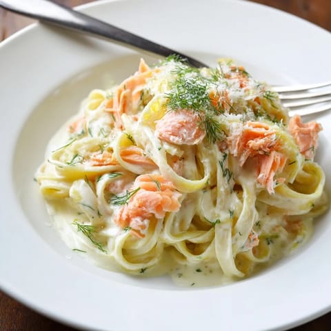 A close-up of creamy salmon pasta topped with Parmesan and fresh dill, served steaming hot in a white bowl.