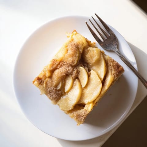 A rustic Dutch-inspired Baked Apple Cake, warm from the oven, showcases cinnamon-dusted apples in a golden, comforting cake served with a dollop of crème fraîche.  