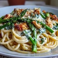 Golden roasted asparagus with crispy Asiago cheese rests atop creamy Asiago chicken linguine, ready to serve for dinner.